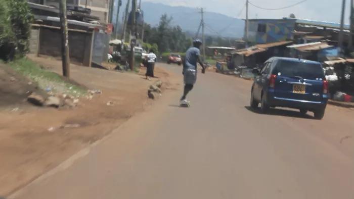 A blurry shot of a longboarder on a busy bypass, with cars visible in the background