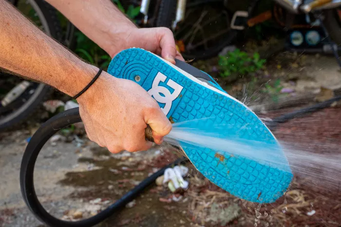 A close-up of the DC x Utmost Lynx OG skate shoe being cleaned with a hose, demonstrating the ease of removing the dog poop.