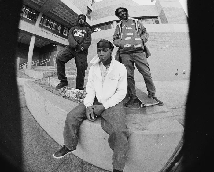 A close-up shot of two members of Public Housing Skate Team, emphasizing their fashion and the gritty urban backdrop.