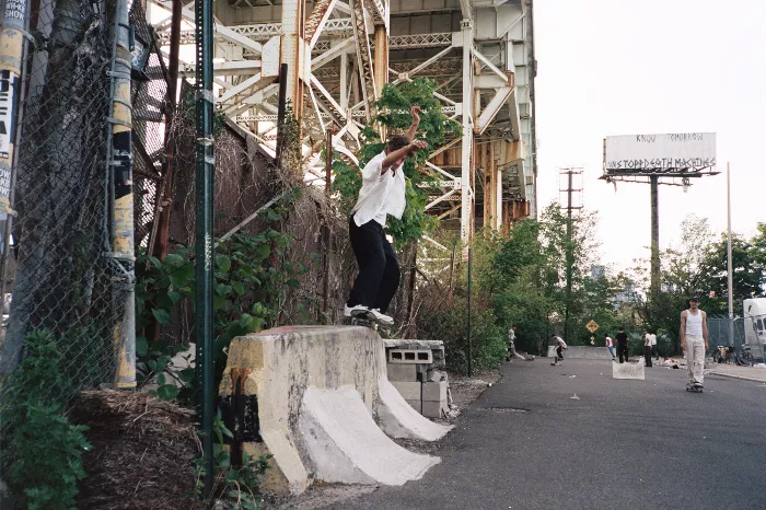 A group of skateboarders at a DIY skate spot featuring ramps and other obstacles, with some holding their boards.