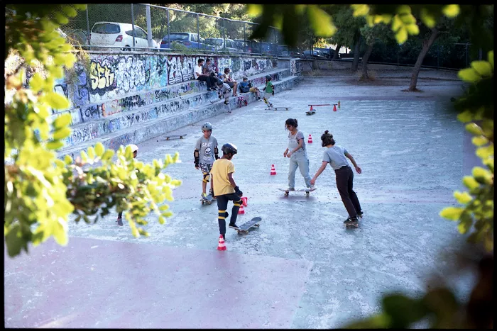 A group of young people skateboarding in a refugee camp, with several people watching in the background