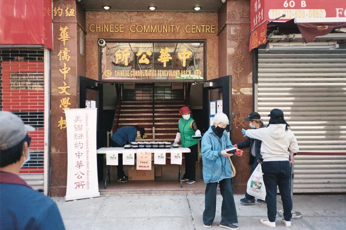 A long line of people extends down a city street, many standing outside a building with signs and posters.