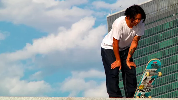 A long shot of Julian Lewis skateboarding on a brick surface on Roosevelt Island with surrounding buildings and construction in the background