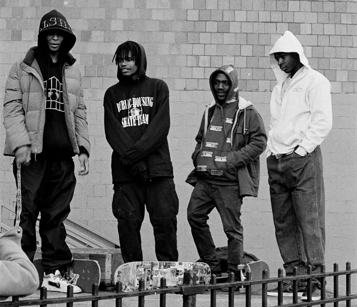 A long shot of three Public Housing Skate Team members skating through an urban environment, showcasing their skills and the unique character of their neighborhood.