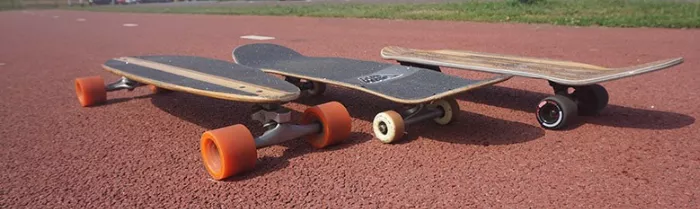 a longboard, skateboard, and cruiser lined up on a paved surface, showcasing their different shapes and sizes