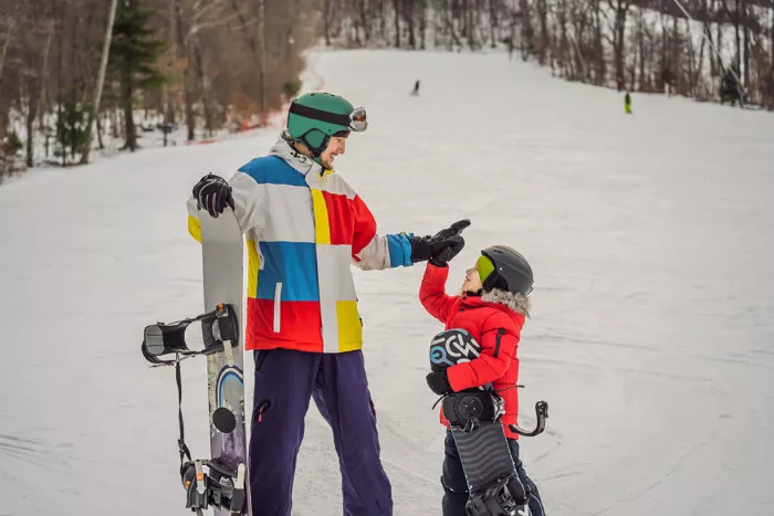 A man and a child wearing snowboarding gear give each other a high five in the snow.