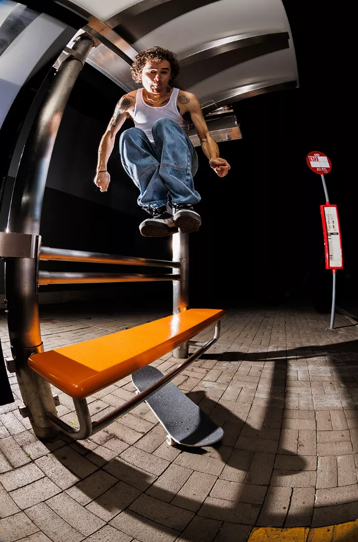 A skateboarder performs a trick on a ledge in a Hong Kong alleyway, with a colorful wall in the background