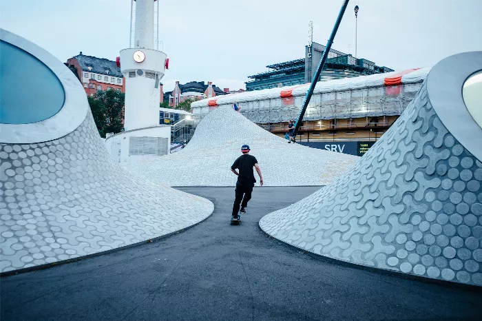 A skater performs a trick at the Helsinki event, with other skaters and obstacles in the background