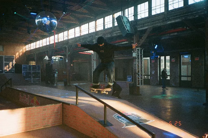 A wide shot of the indoor skatepark, featuring ramps and obstacles, with skaters in the background