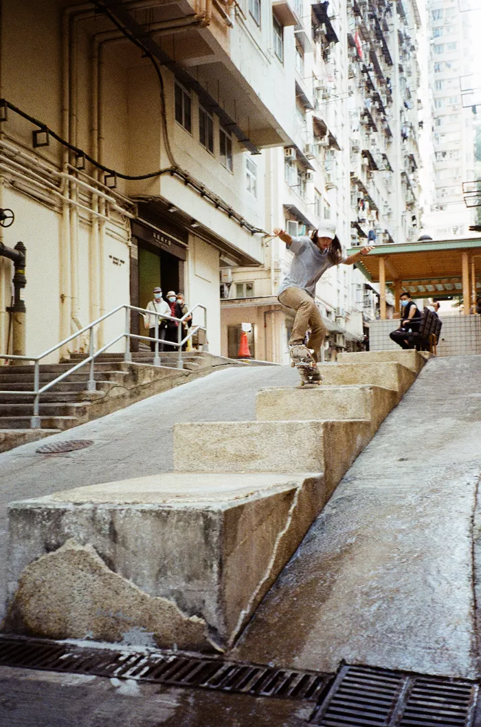 A wider shot of skateboarders skating on a public urban area, with high buildings in the background