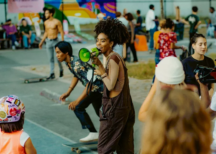 Briana King, a Black woman, sitting on the ground in a skatepark, smiling and looking directly at the camera, with a skateboard beside her.