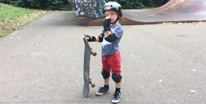 child wearing full protective gear and holding a skateboard