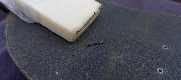 Close up of a hand cleaning a longboard grip tape with a belt sander cleaner