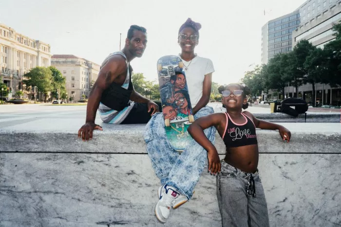 Demi Harper executing a skateboard trick while being observed by her father, Darren Harper, at Freedom Plaza.