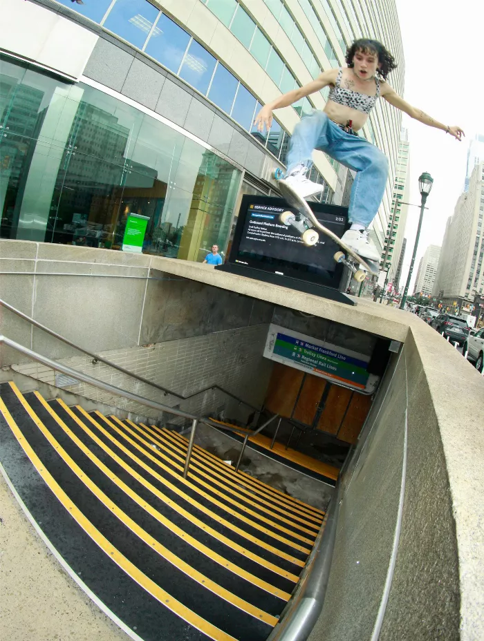 Efron Danzig performing a trick on a skateboard, with a subway entrance in the background.