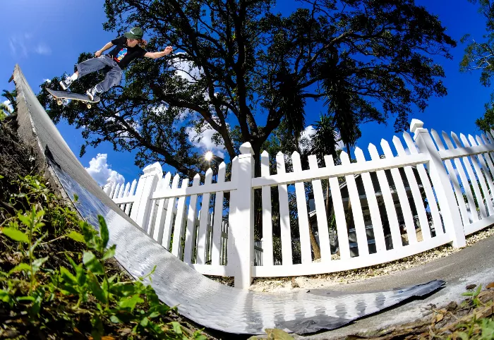 Jake Fuscardo executes a nollie half-cab on a longboard. The photo captures the skater in mid-air against a somewhat blurry background.