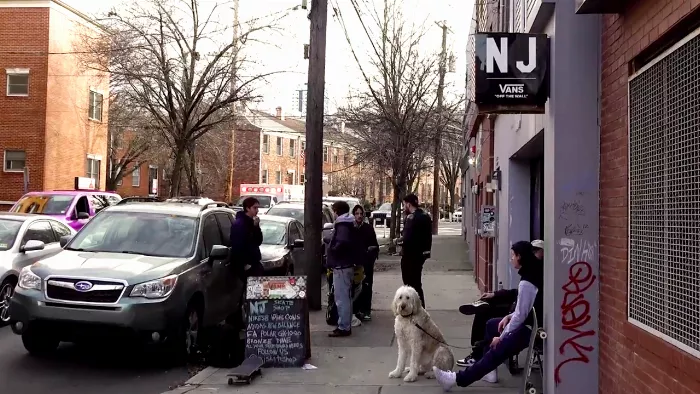 Several people are sitting and standing in what appears to be a skate shop. Some of them are looking at the camera.