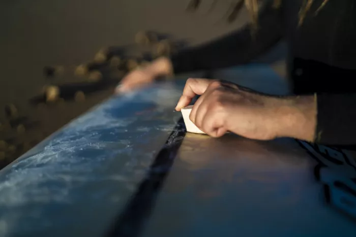 Surfer applying wax to a surfboard deck