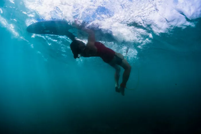 Surfer performing a turtle roll underwater, with the board above their head and their body submerged, showcasing the technique in action.