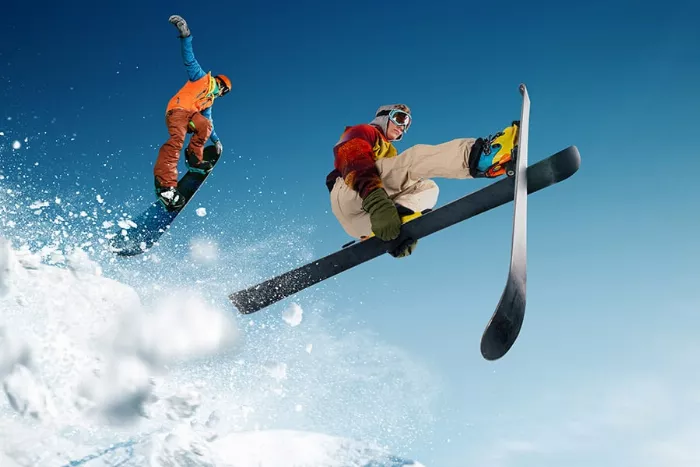 Two people snowboarding and skiing down a snowy slope