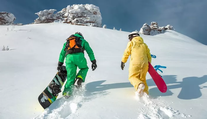 Two snowboarders hiking up a snowy slope